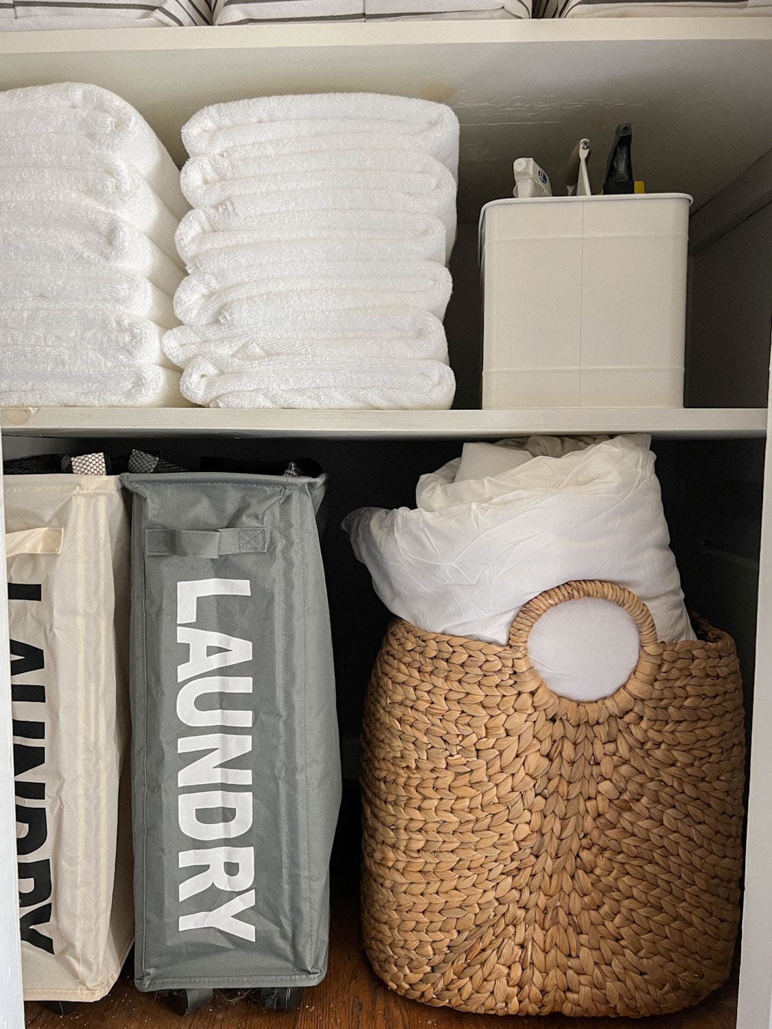 back of white towels on bathroom linen closet shelving with cleaning caddy and laundry. hampers