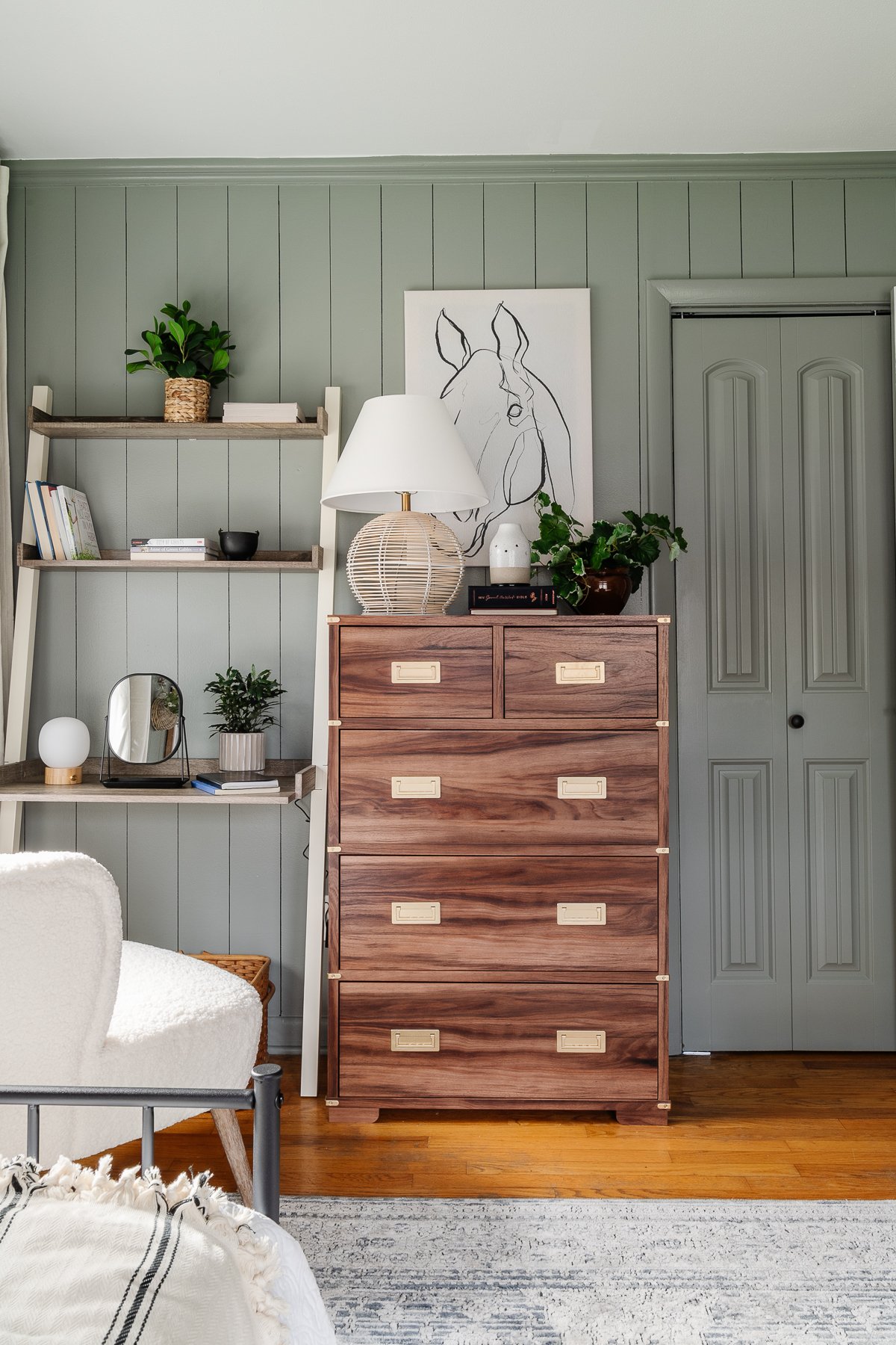 sage green bedroom with wood dresser, leaning desk, and white boucle desk chair