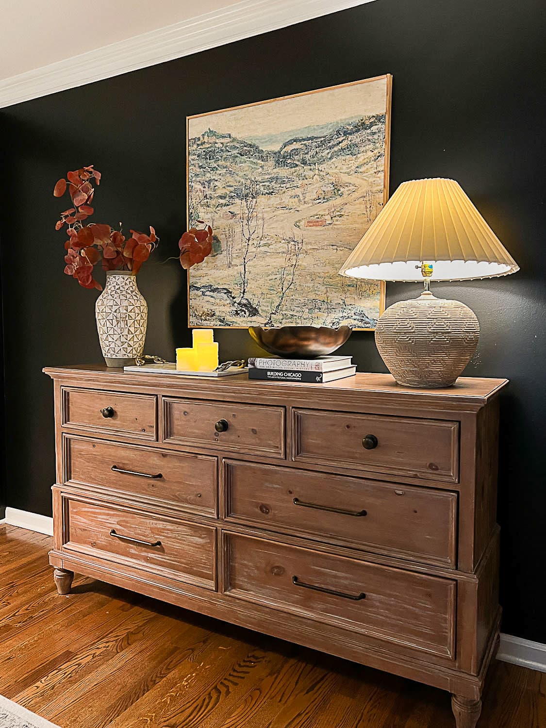 dresser decor in a bedroom with lamp, art, and vase of branches