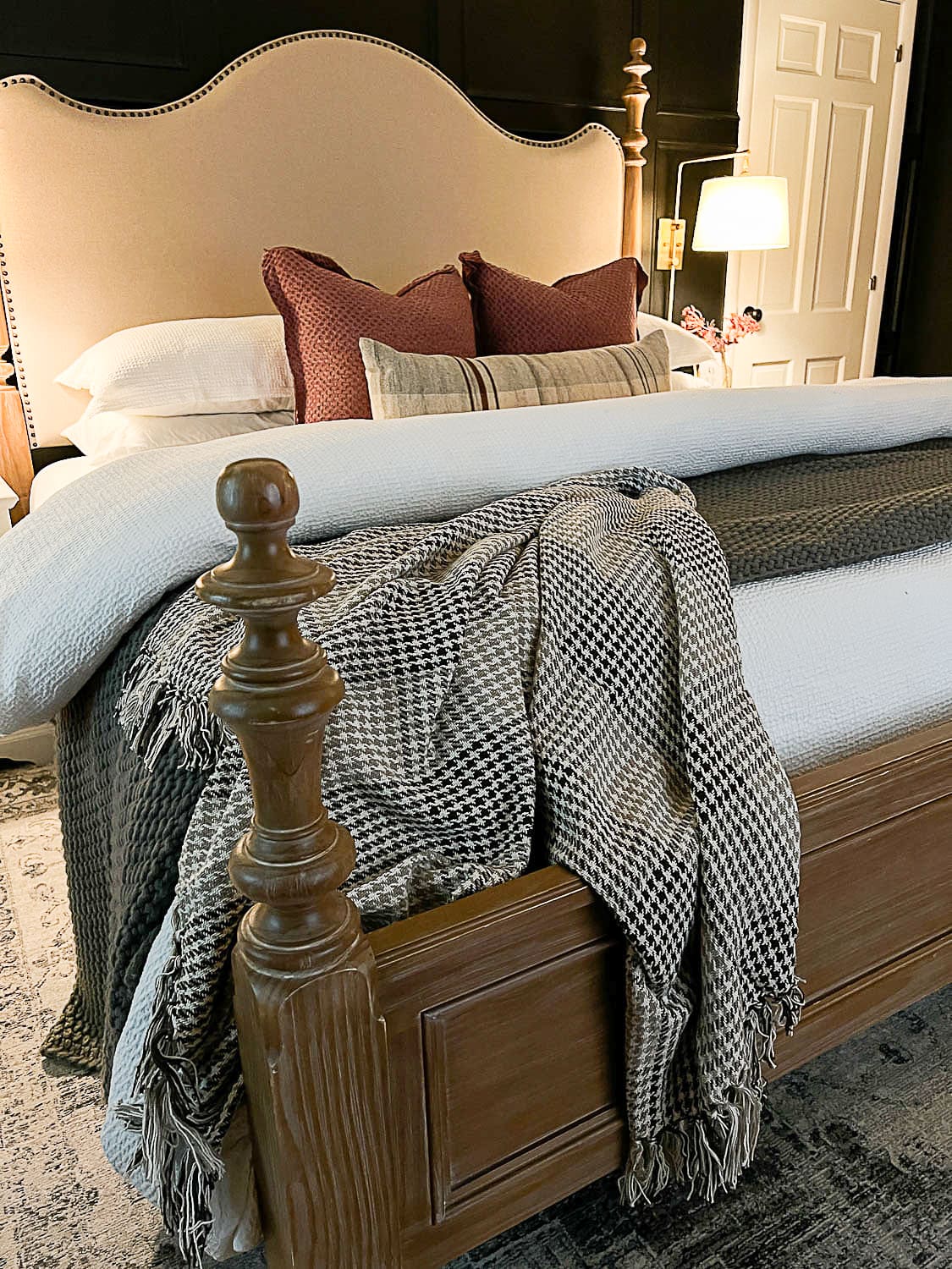 wood and upholstered bed with mauve pillows and houndstooth blanket