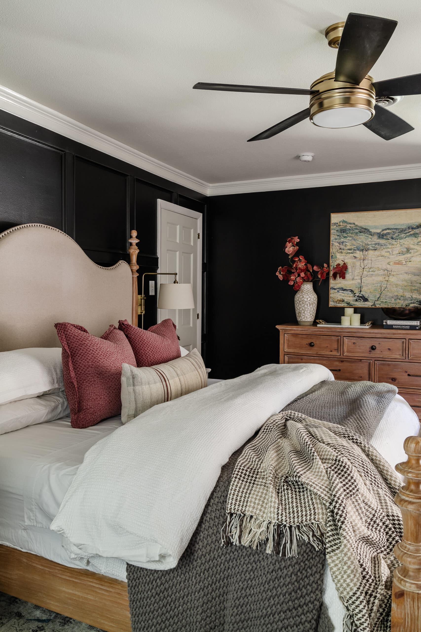 cozy bedroom with black walls, comfy bedding, and wooden dresser
