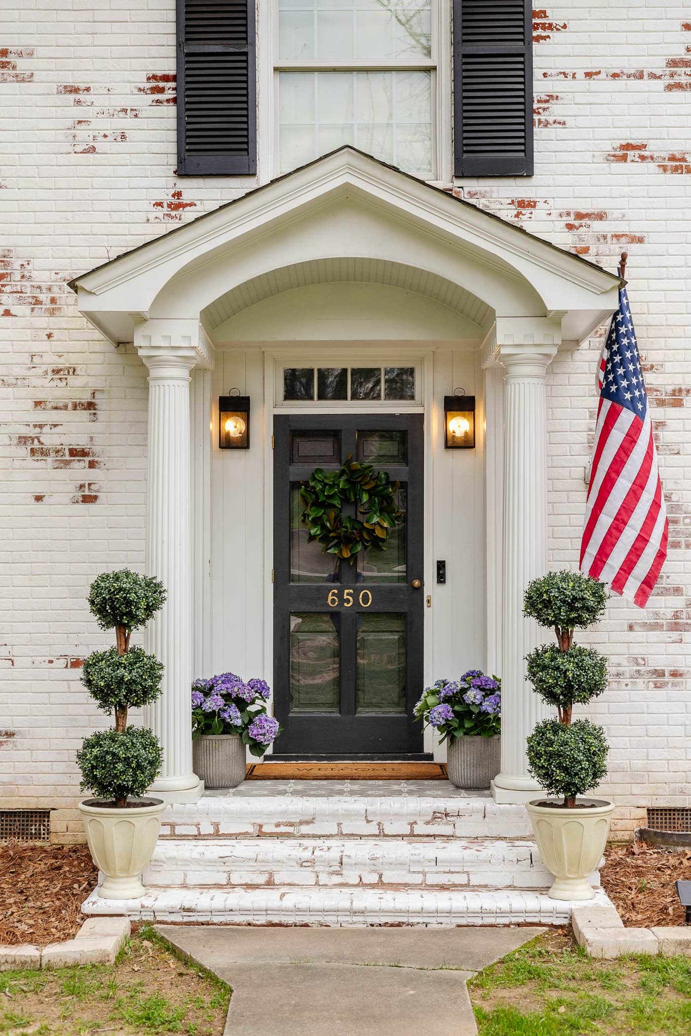 colonial small front porch on a limewashed brick house with boxwood topiaries and hydrangeas in planters 