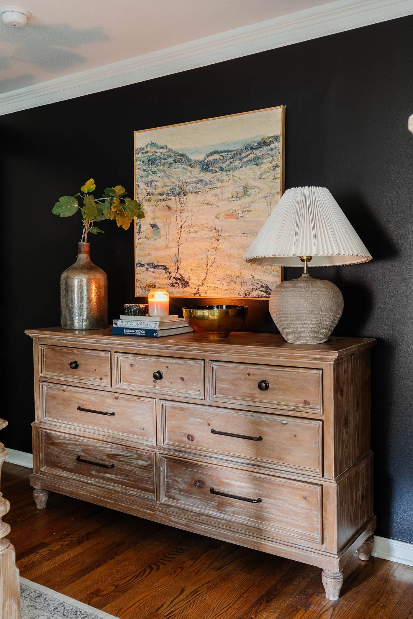 winter bedroom decor on a dresser with lamp, art, candle, and vase of greenery