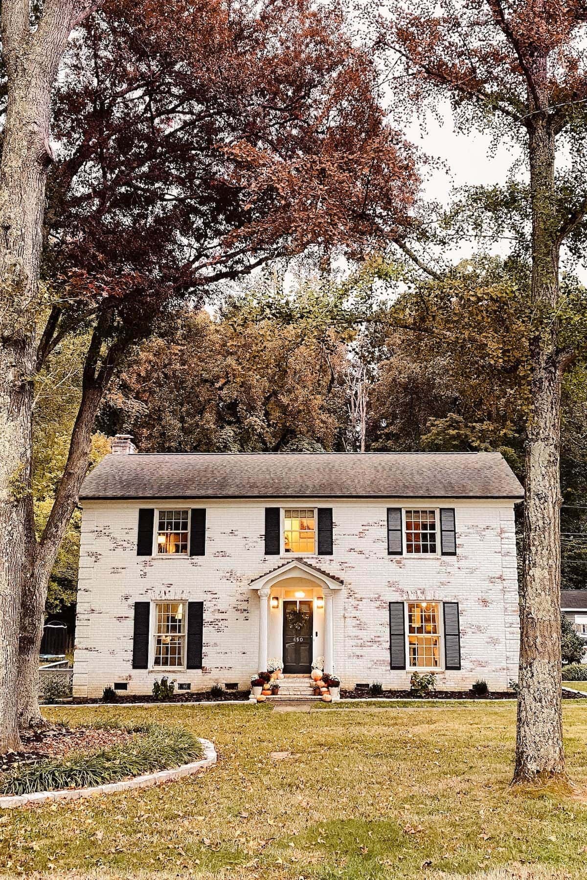 limewashed brick colonial house decorated for fall with pumpkins and mums