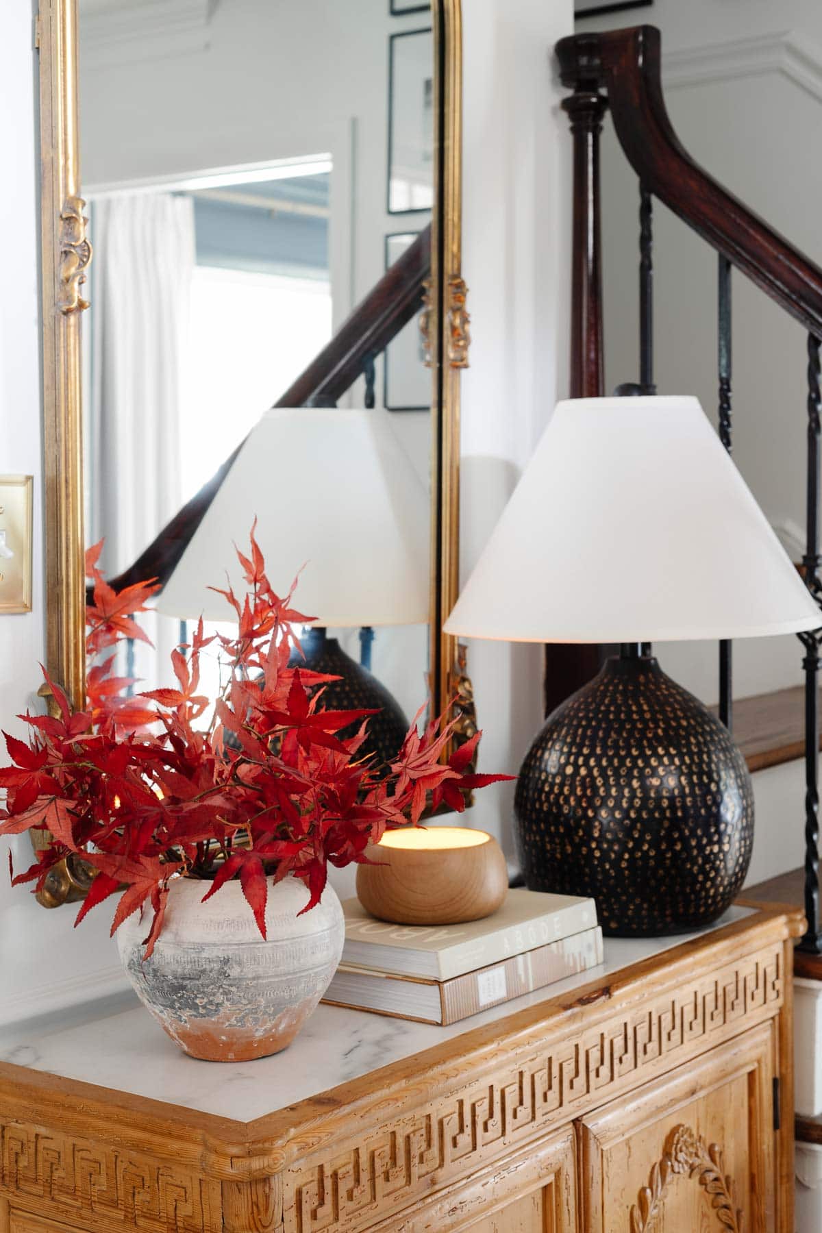 entry table with table lamp, terracotta vase of fall leaves, and wood cabinet