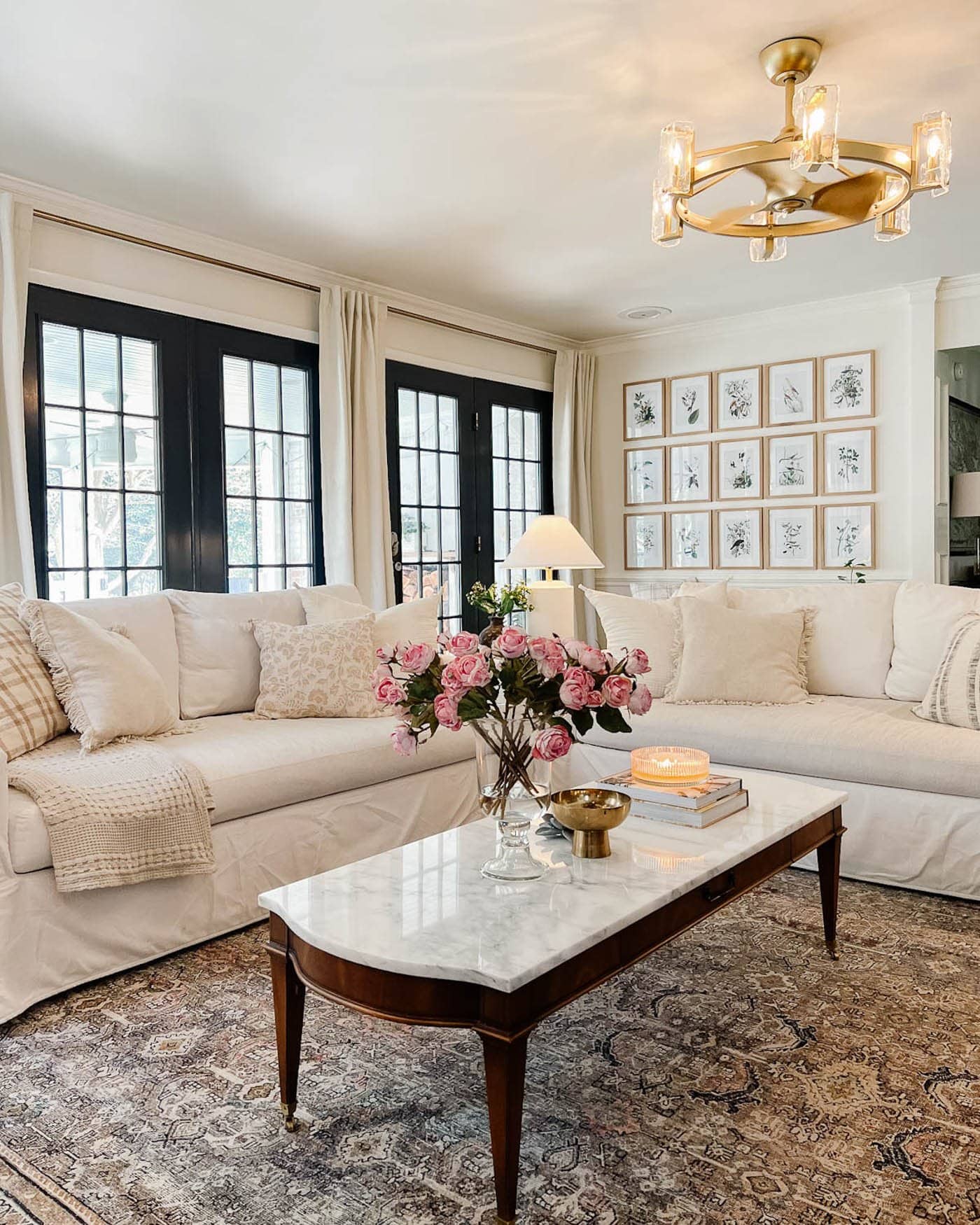 living room with white walls, black French doors, and white sofas with a rug and marble topped coffee table