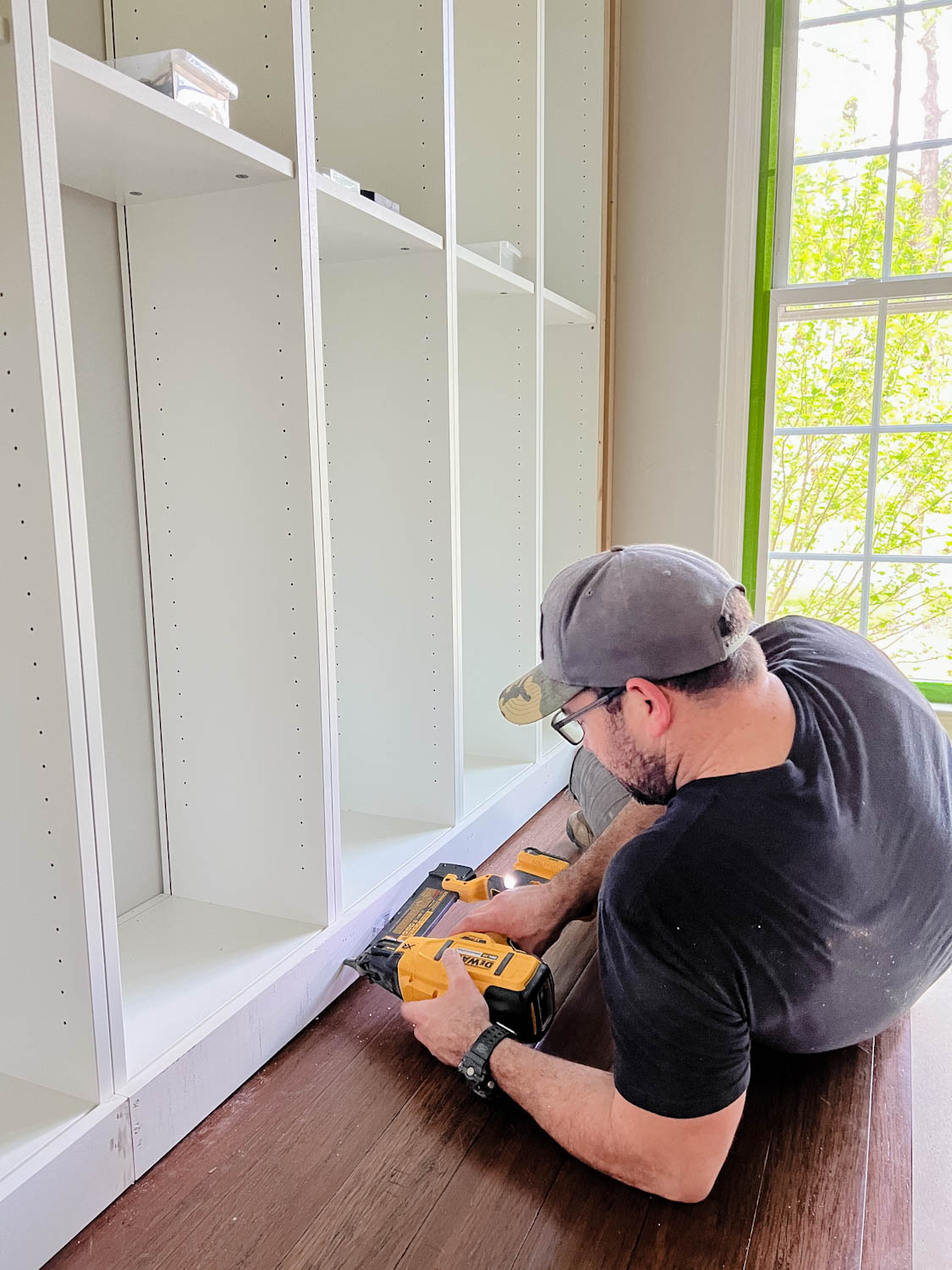 attaching 1x4 board to the bottom of bookcases using a finish nailer for DIY built in bookshelves