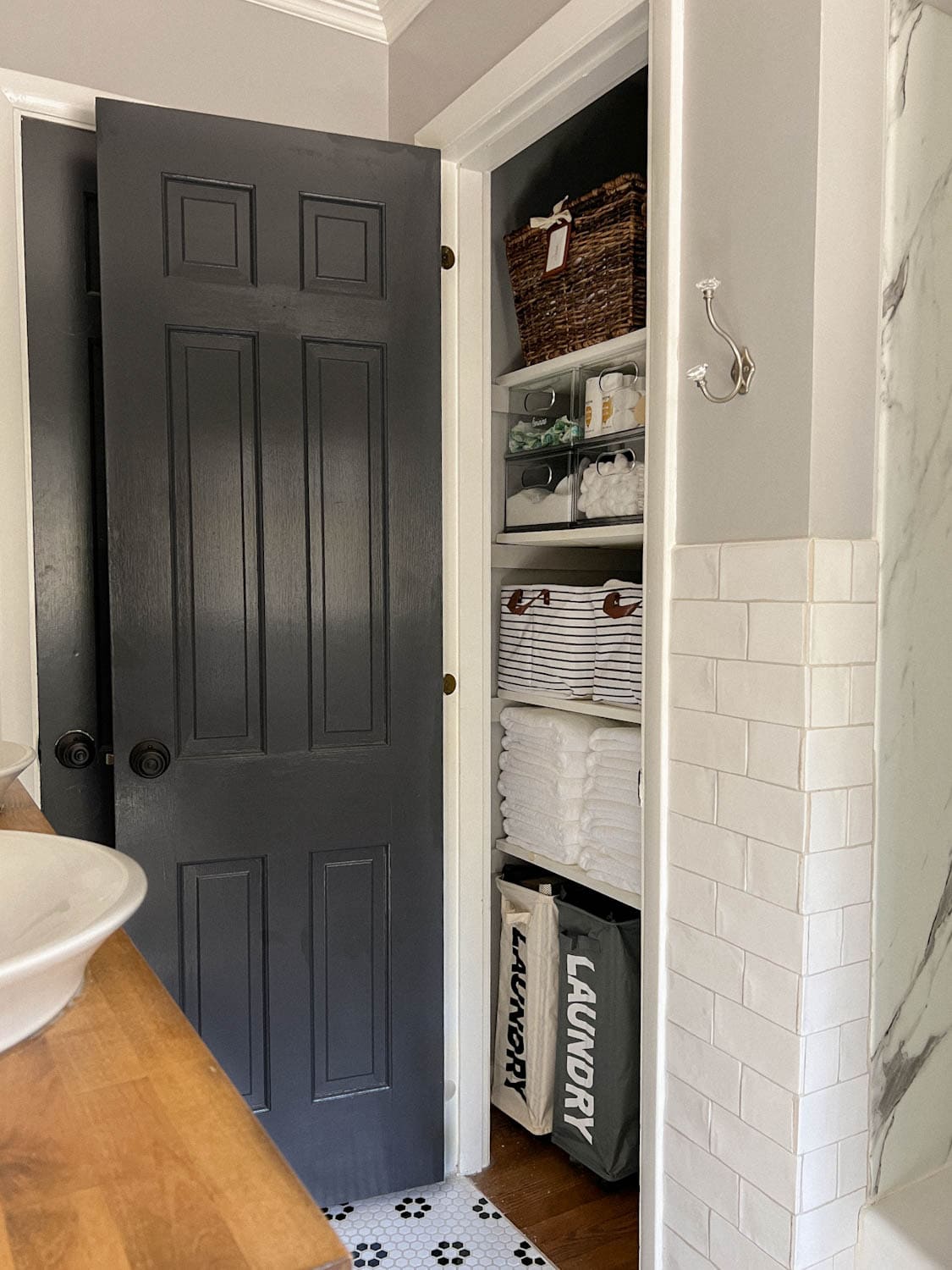 linen closet in a bathroom with black door, white tile, and gray walls