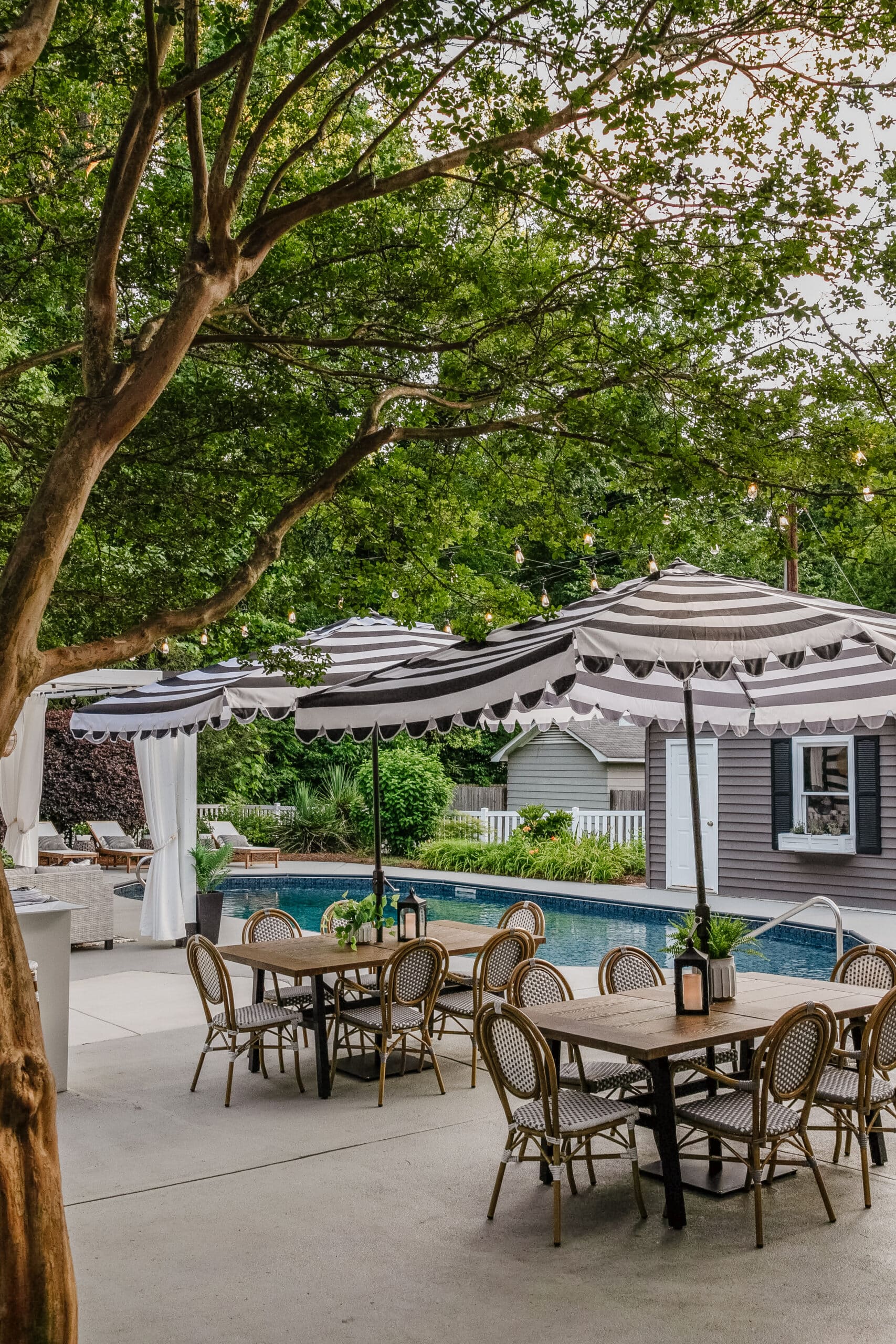 patio dining tables and chairs with striped umbrellas for shade around a backyard pool