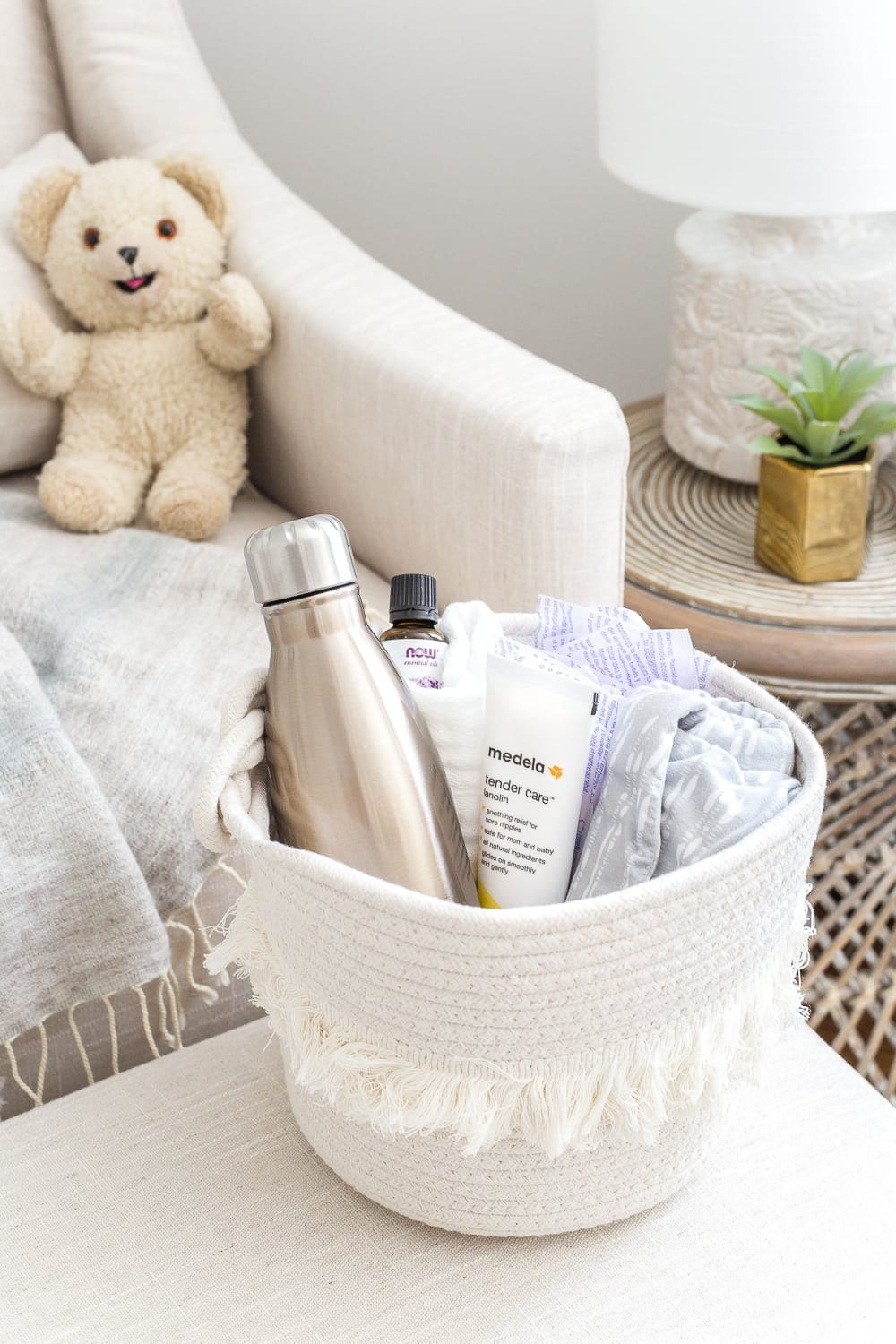 Nursery Organization | Breastfeeding basket to keep beside a chair filled with nursing pads, water bottle, lanolin, burp cloths, nursing cover, and lavender essential oil.